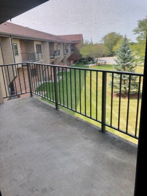 A view from a balcony overlooking a lawn and trees in a residential area.