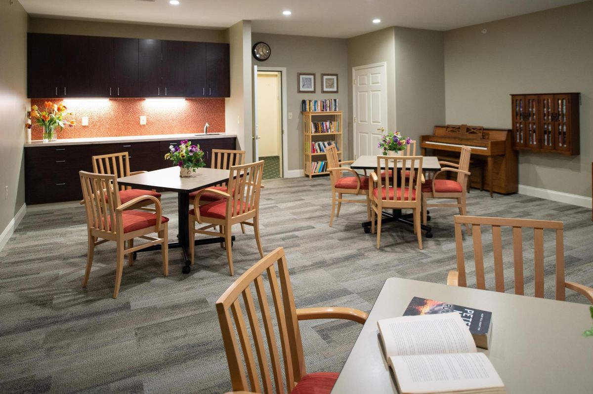 A cozy room with tables and chairs, featuring a bookshelf and a piano.