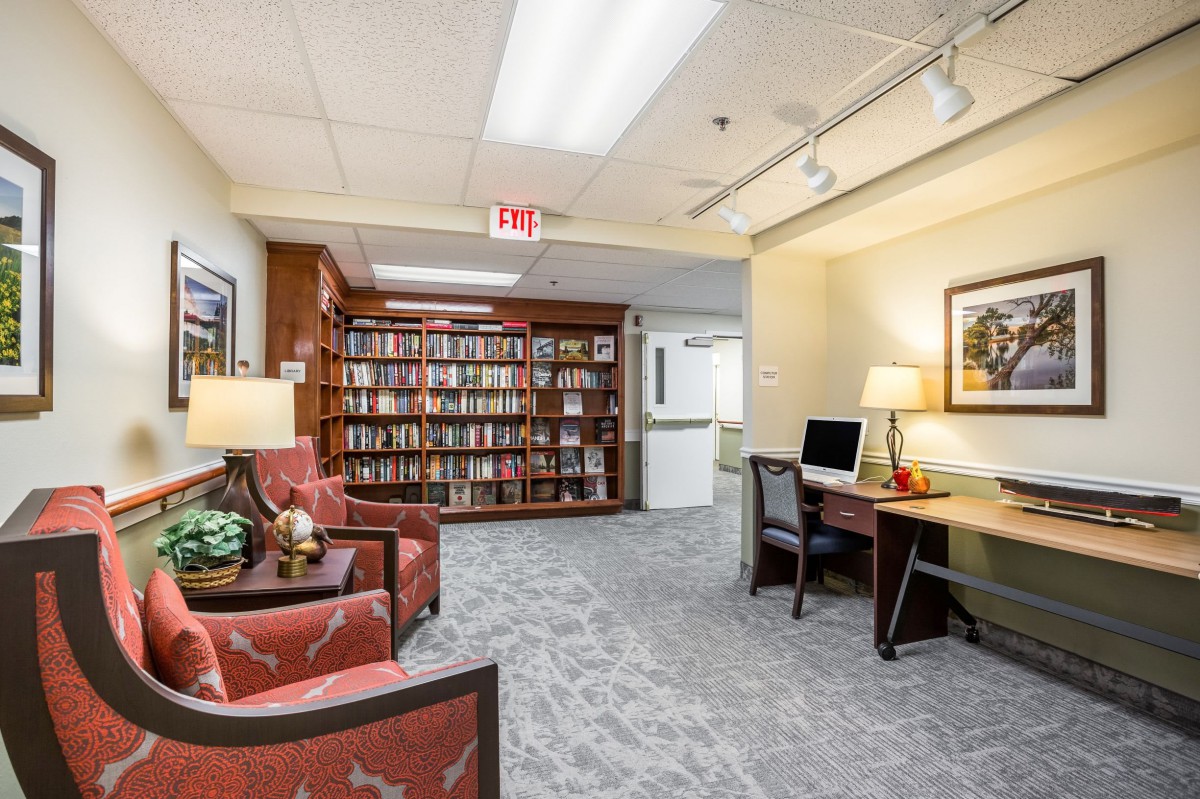 A cozy library interior with bookshelves, armchairs, and a computer desk.