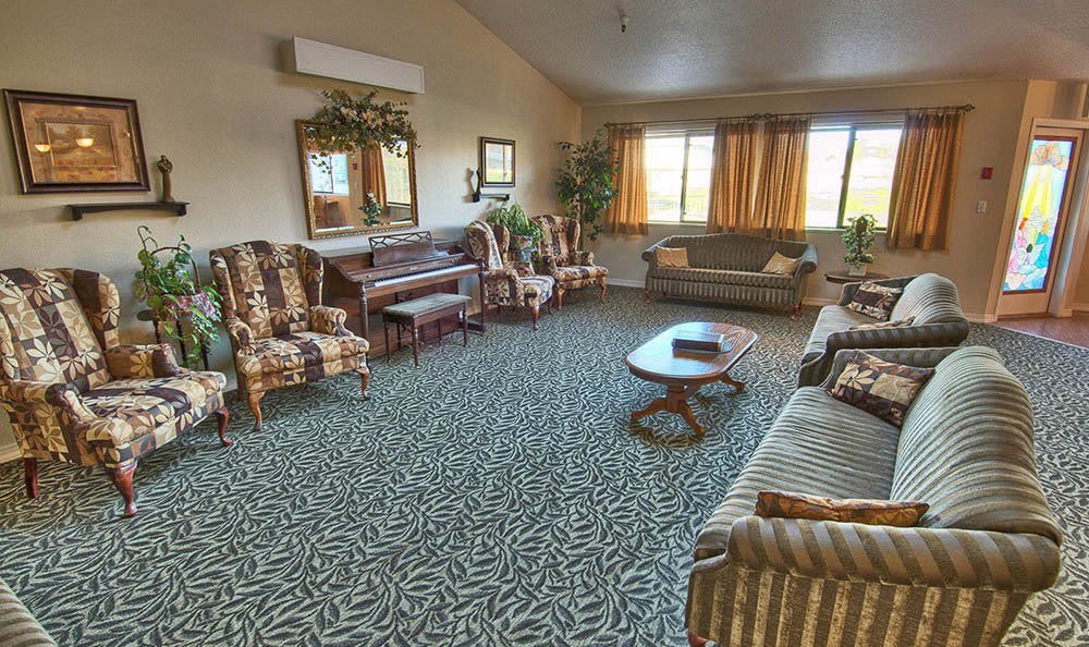 A spacious living room with patterned carpet, comfortable seating, and a piano.