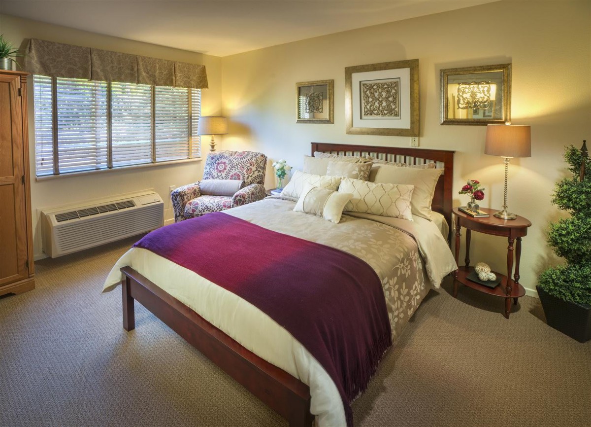 A cozy bedroom interior with a neatly made bed, decorative pillows, and warm lighting.