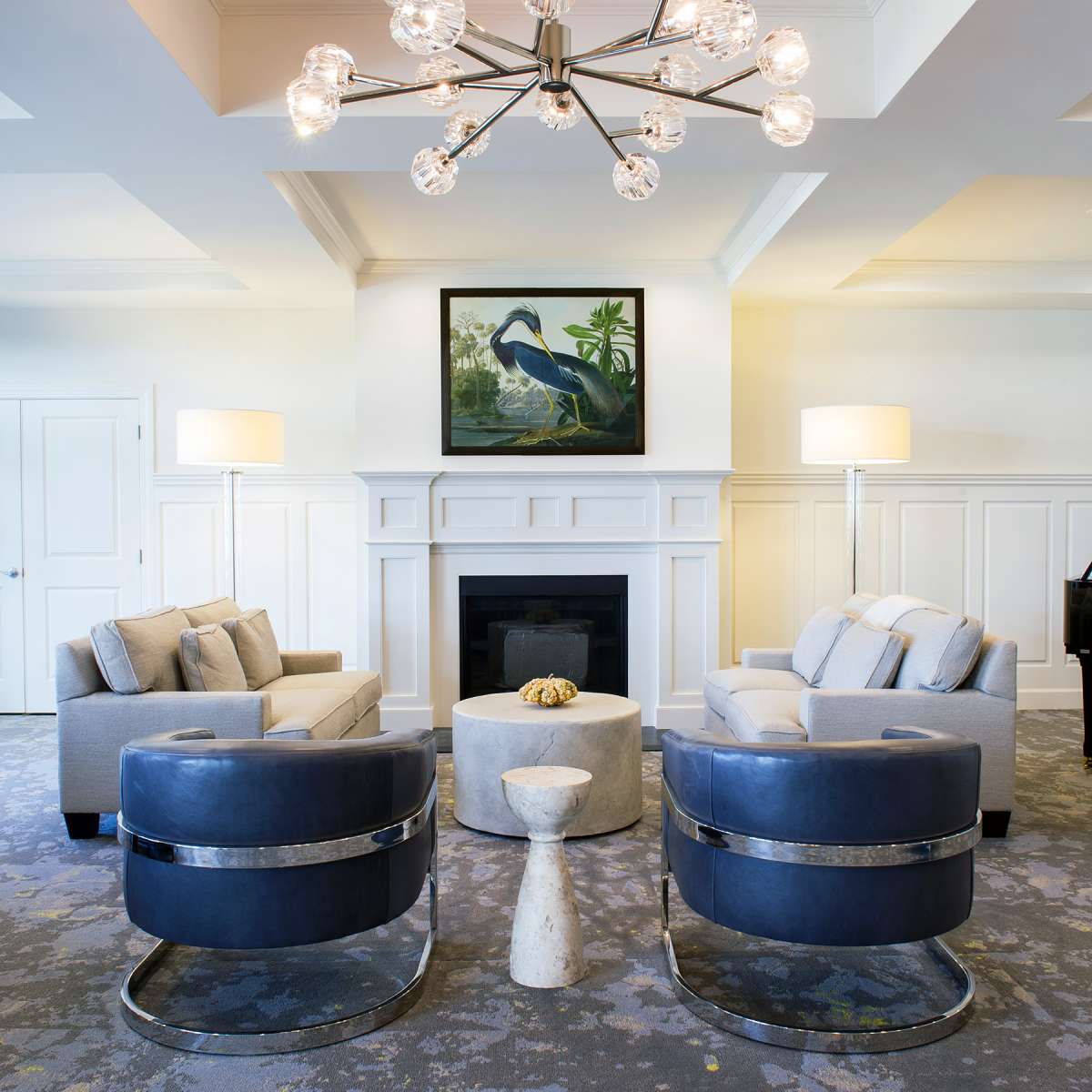 A modern living room with stylish furniture and a central fireplace, adorned with a contemporary chandelier and artwork on the wall.