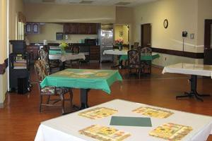 An empty dining room with tables and chairs set up, adjacent to a kitchen area.