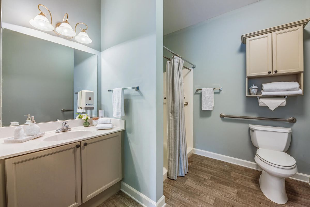 A modern bathroom featuring a sink, mirror, shower, and toilet with organized toiletries and towels.