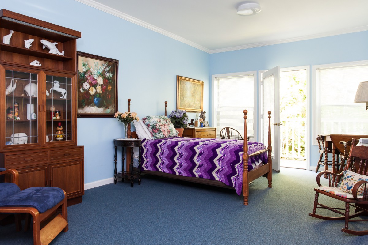 A cozy bedroom with a wooden bed and purple blanket, light blue walls, and decorative paintings.