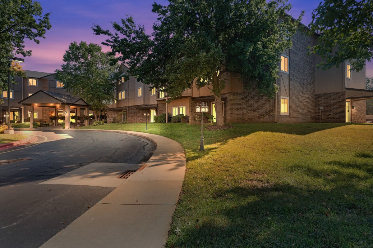 A nighttime view of a building with lit windows, surrounded by trees and grass.