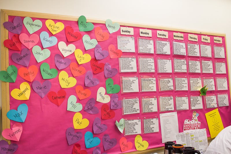 A classroom bulletin board decorated with colorful heart-shaped notes and a weekly schedule.