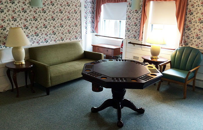 A cozy living room with a vintage poker table, green sofa, and a lamp near the window.