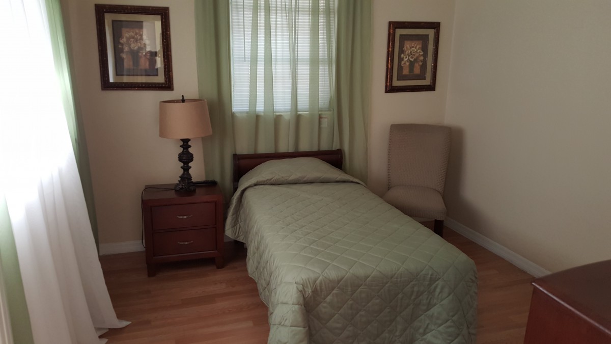 A cozy bedroom with a single bed, nightstand with lamp, and framed pictures on the wall.