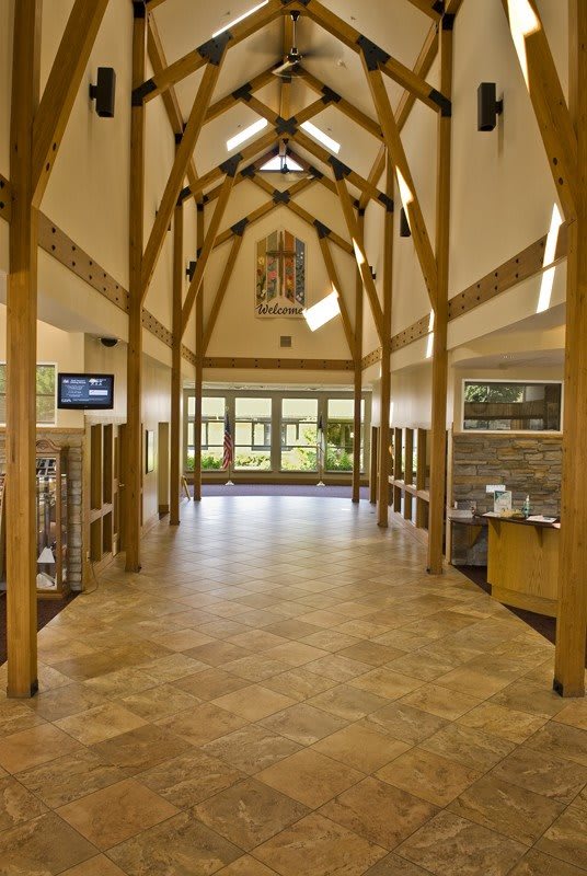 A spacious, well-lit hallway with wooden beams and large windows.