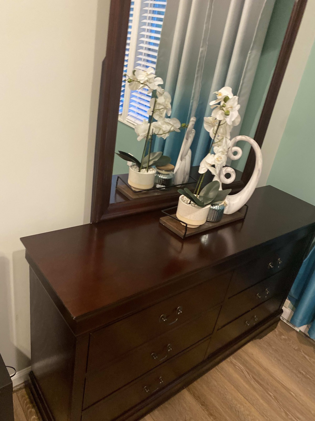 A wooden dresser with a mirror, adorned with a vase of flowers.
