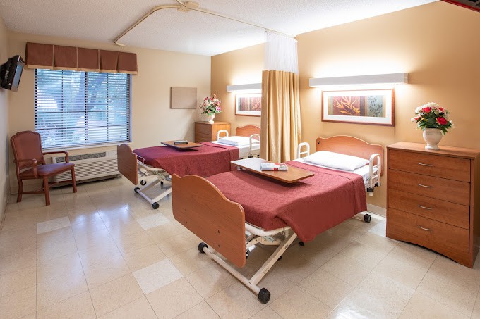 A hospital room with two beds separated by a curtain, featuring medical equipment and a large window.
