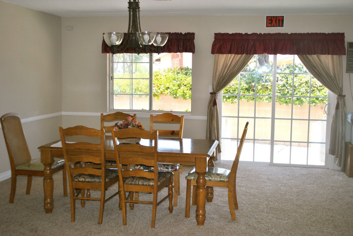 A dining room with a wooden table set and large windows letting in natural light.