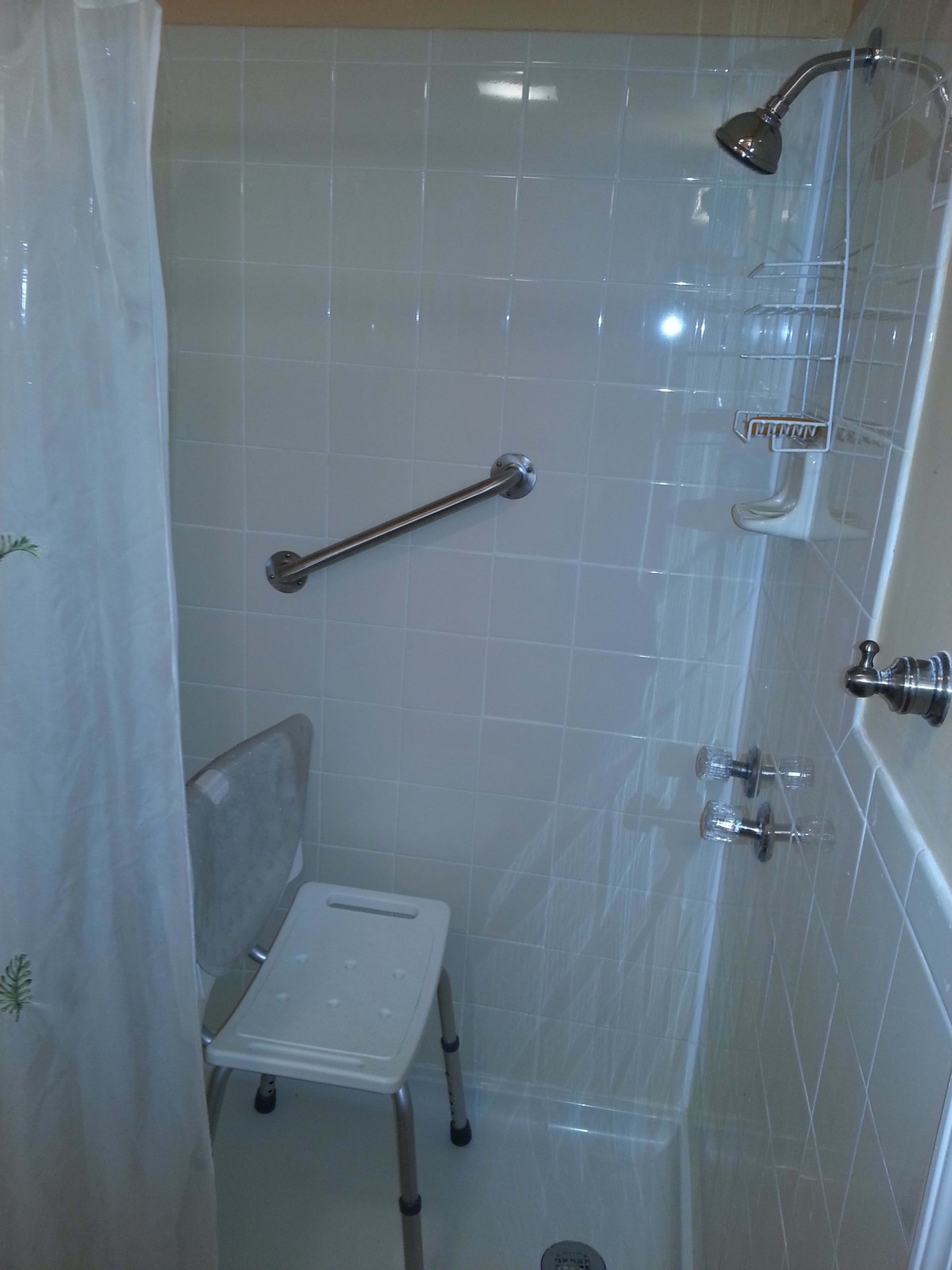 A bathroom shower with a grab bar and shower chair.