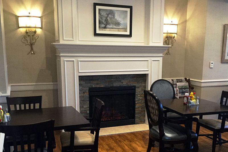A cozy dining area featuring a white fireplace, surrounded by tables and chairs.