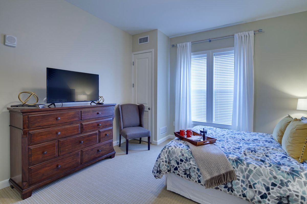 A cozy bedroom with a bed, dresser, television, and large window with curtains.