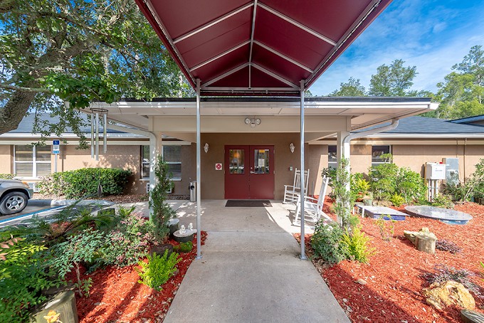 An entrance to a building with a red canopy, surrounded by landscaped gardens.