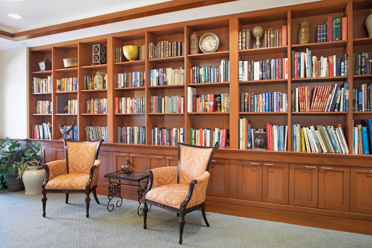 A cozy library with wooden bookshelves filled with books and two comfortable chairs.
