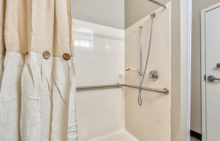 A bathroom shower with a curtain, grab bar, and wall-mounted shower head.