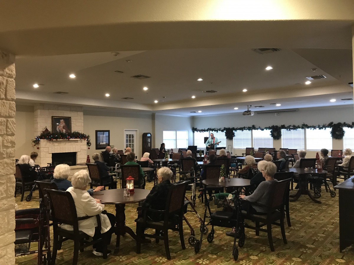A group of elderly people gathered in a community room with tables and chairs.