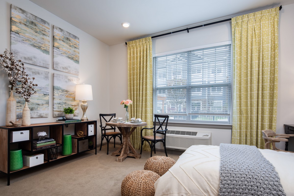 A cozy bedroom with a small dining area, featuring bright yellow curtains and modern decor.