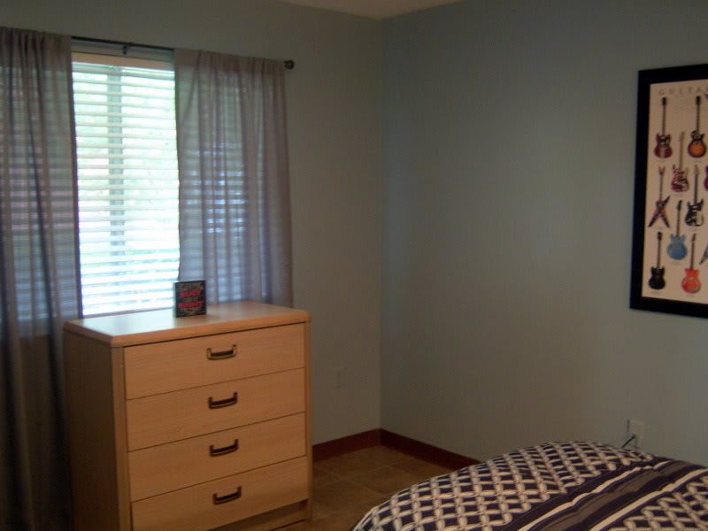 A simple bedroom with a dresser and a window with curtains.
