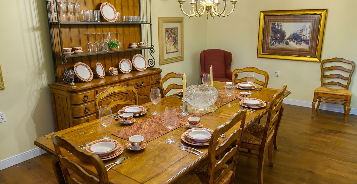 A cozy dining room with a wooden table set for a meal, surrounded by chairs and adorned with a chandelier.