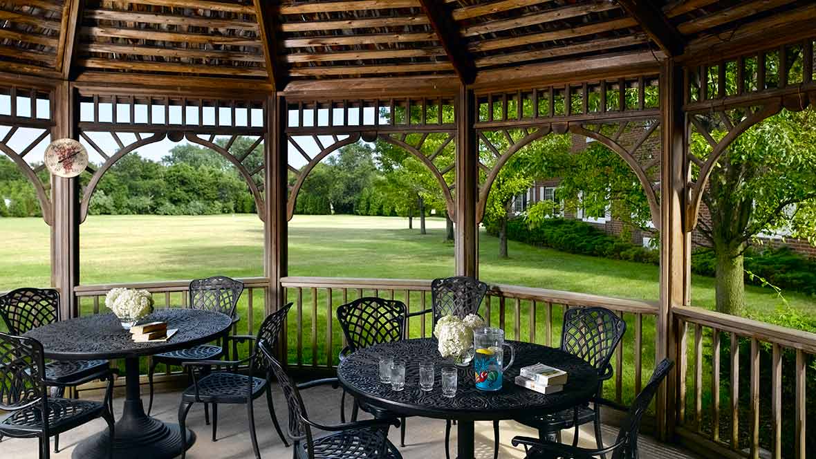 A peaceful outdoor gazebo with tables and chairs overlooking a lush green lawn.