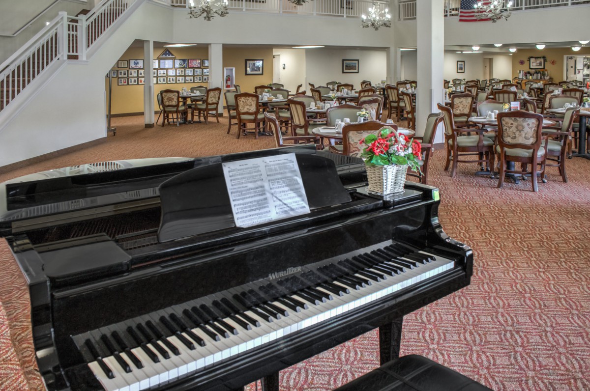 A grand piano with sheet music and flowers on top, located in a spacious dining area.
