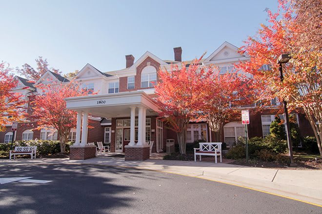 A brick building with a portico entrance, surrounded by trees with vibrant red autumn leaves.