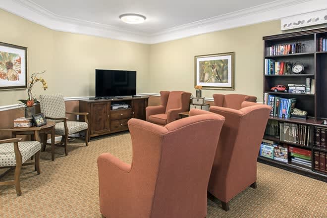 A cozy living room with armchairs facing a television, featuring warm colors and a carpeted floor.