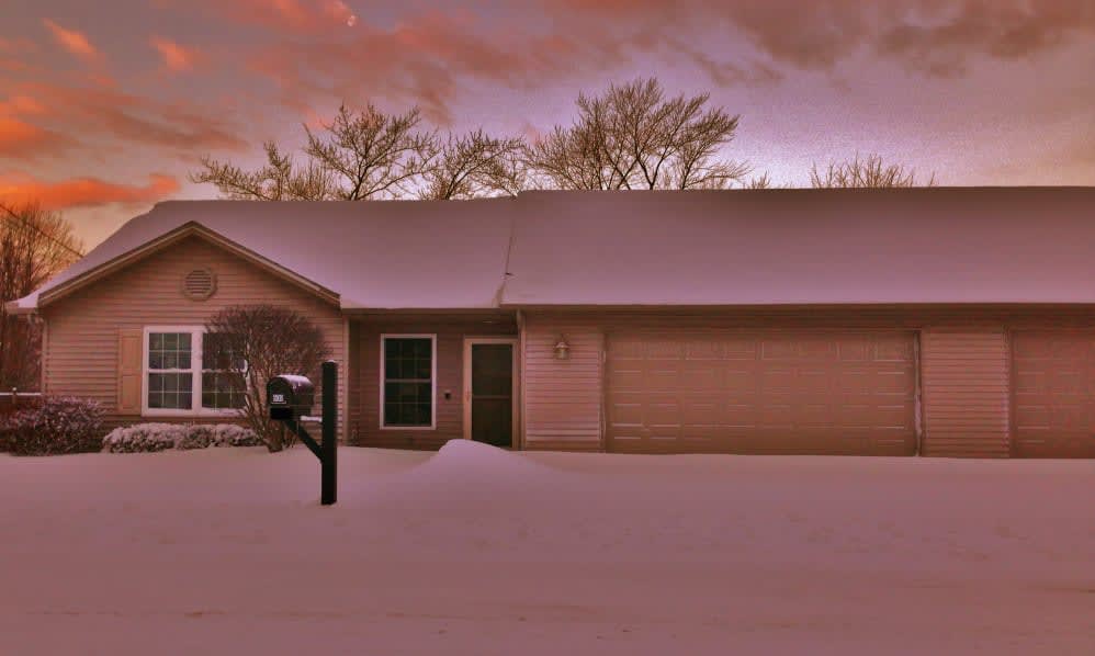 A snow-covered house at sunset with a peaceful winter landscape.
