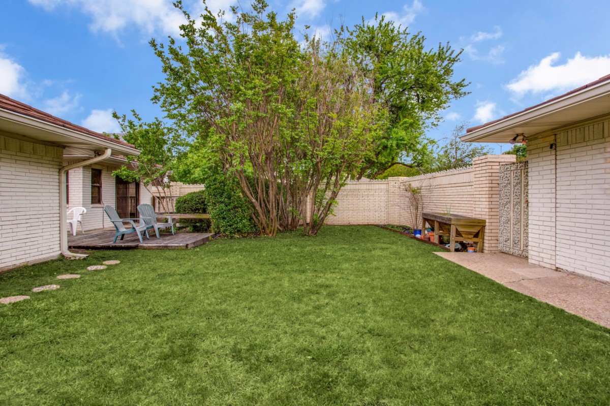 A tranquil backyard with a lush green lawn and surrounding trees, complemented by patio seating for outdoor relaxation.