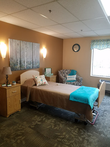 A well-lit hospital room featuring a bed, chair, and warm decor.