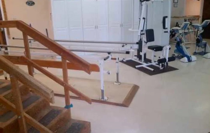 A room equipped with rehabilitation and physical therapy equipment, including parallel bars and exercise machines.
