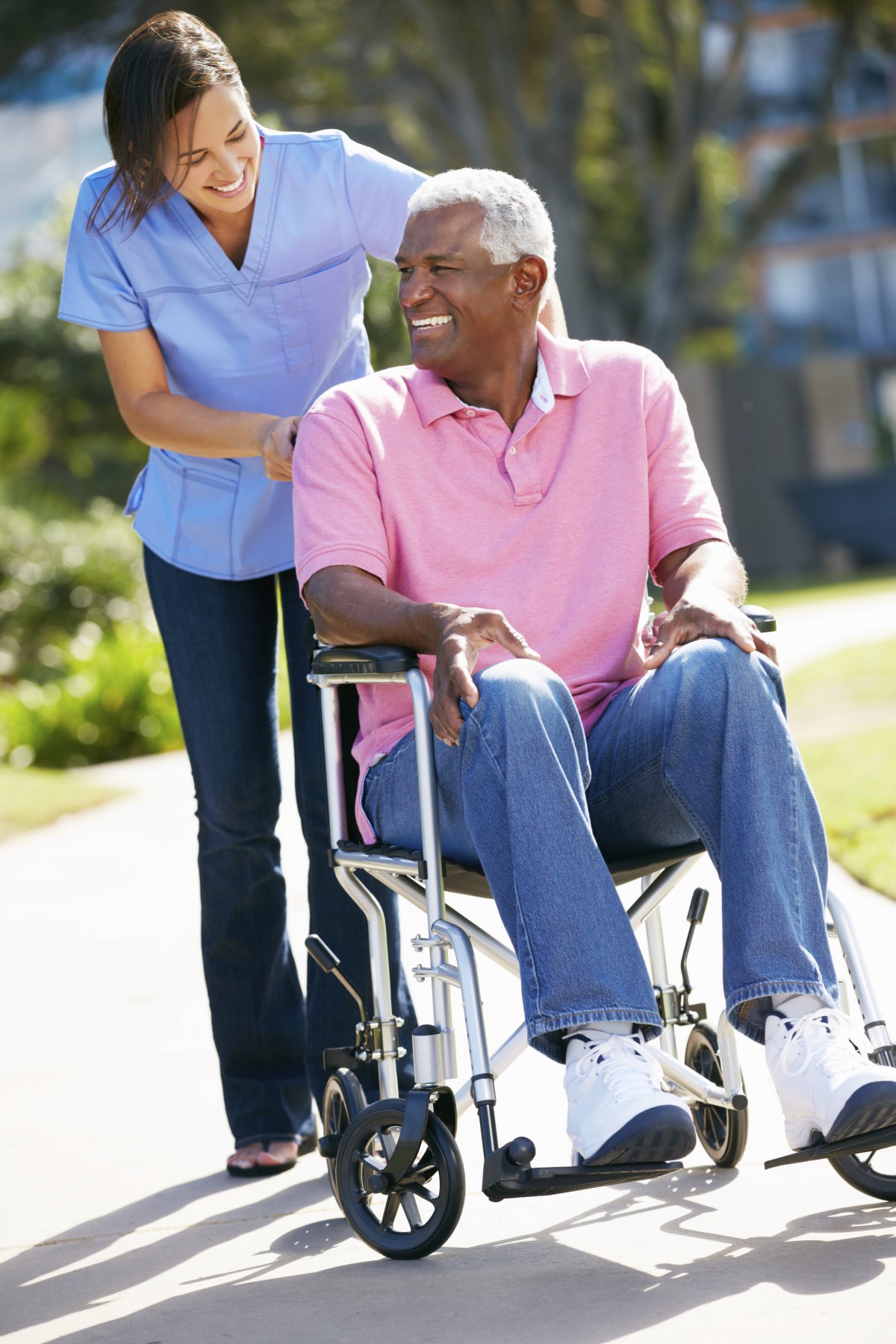 A caregiver assists an elderly man in a wheelchair outdoors.