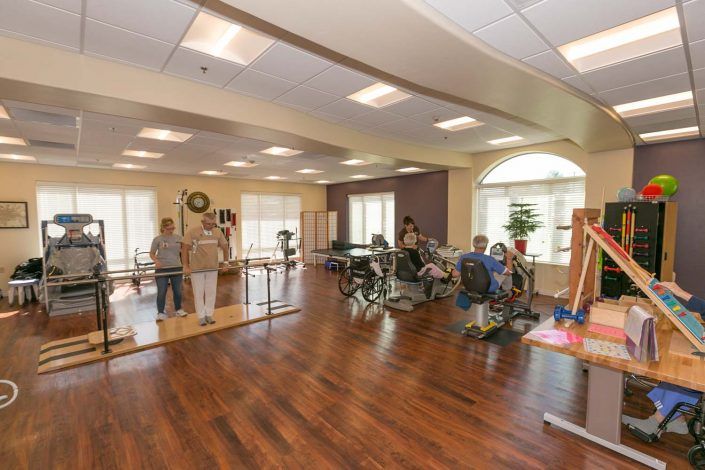 A rehabilitation center with various exercise equipment and patients engaging in physical therapy activities.