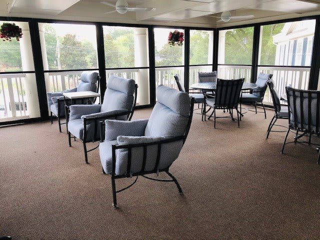 A cozy enclosed patio with cushioned chairs and tables, surrounded by large windows.