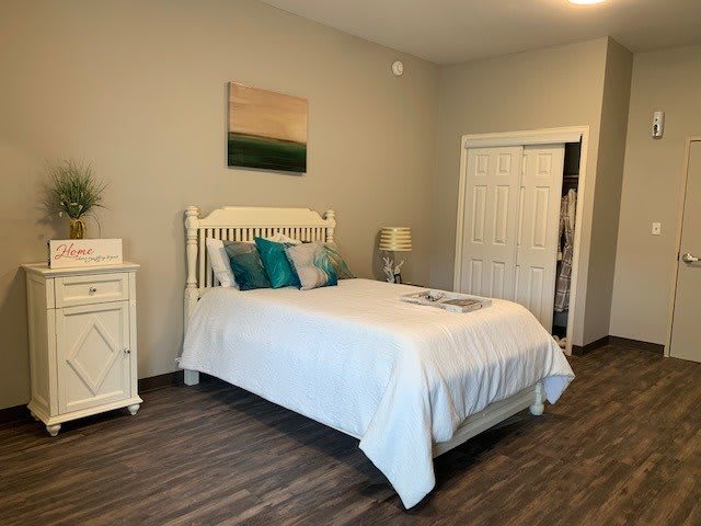 A cozy bedroom featuring a white bed with colorful cushions, wooden flooring, and a neatly decorated interior.