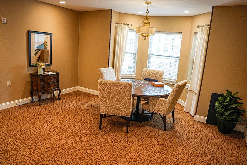 A cozy dining room with a round table and upholstered chairs, featuring a warm color palette and natural lighting from large windows.