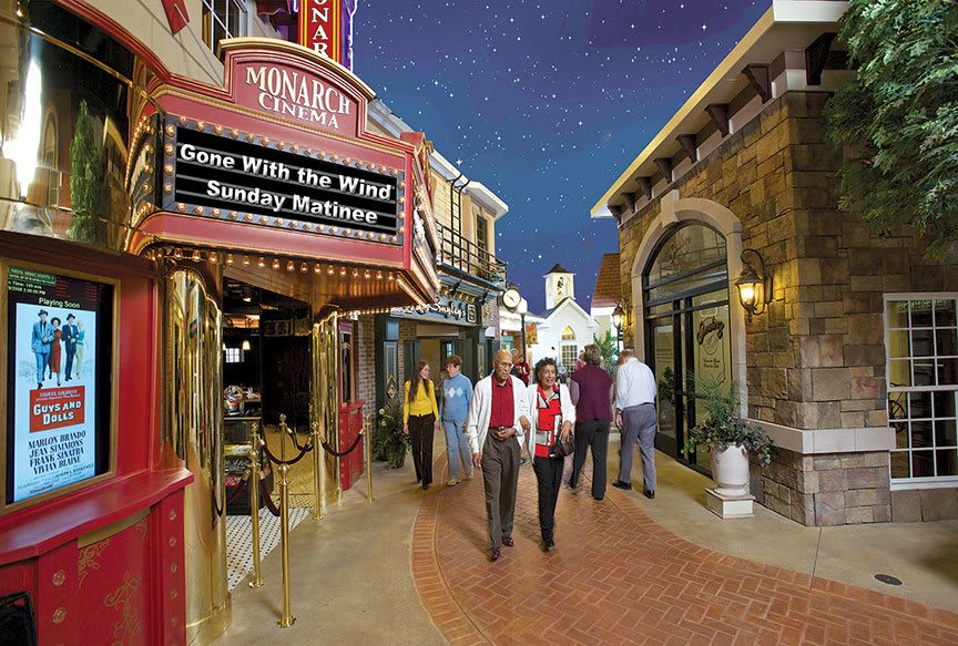 A group of people walking through an indoor shopping area with a theater under a starry artificial sky.