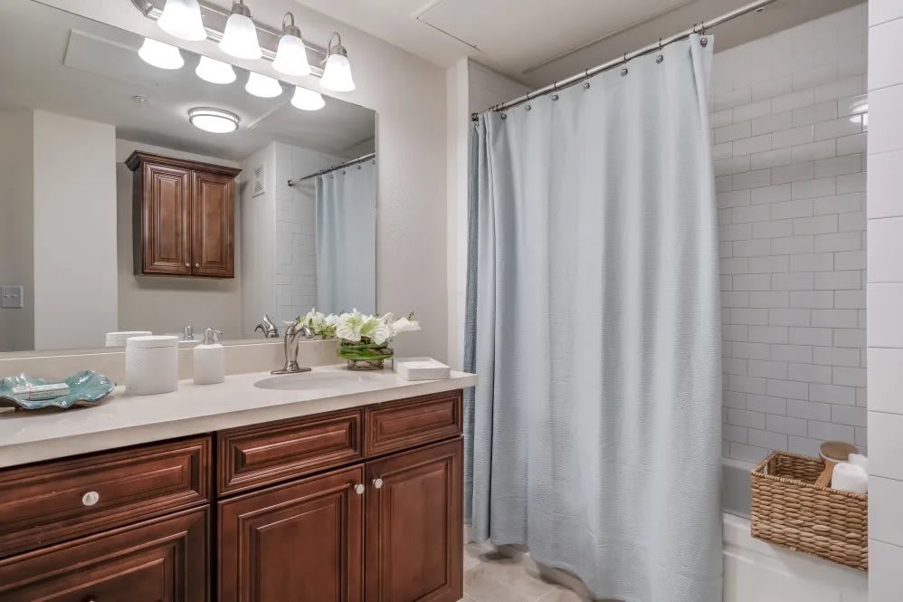 A modern bathroom featuring wooden cabinets, a large mirror, and a light blue shower curtain.