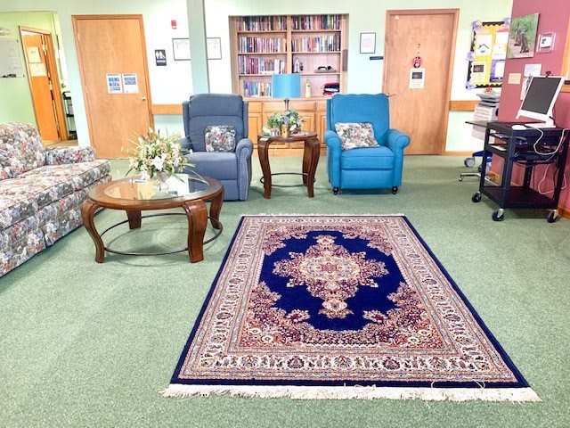 A cozy living room area with armchairs, a patterned rug, and bookshelves in the background.