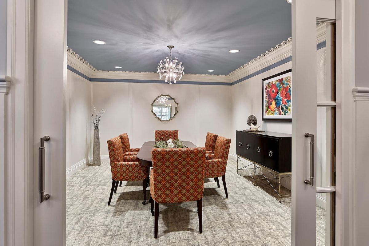 A stylish dining room with a chandelier, colorful artwork, and upholstered chairs.