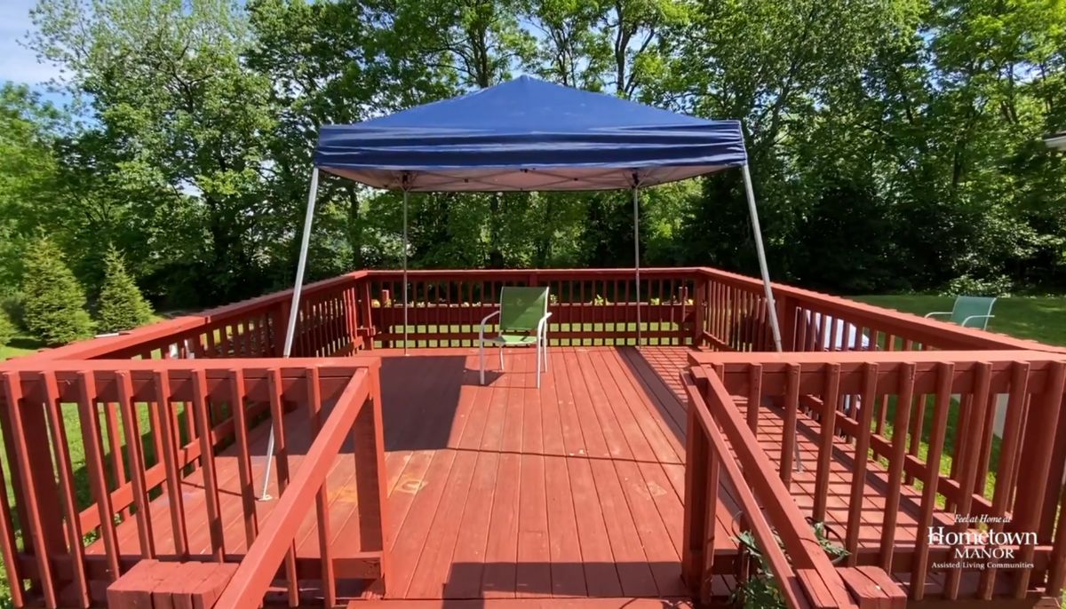 A sunny outdoor deck with a blue canopy and a single chair.