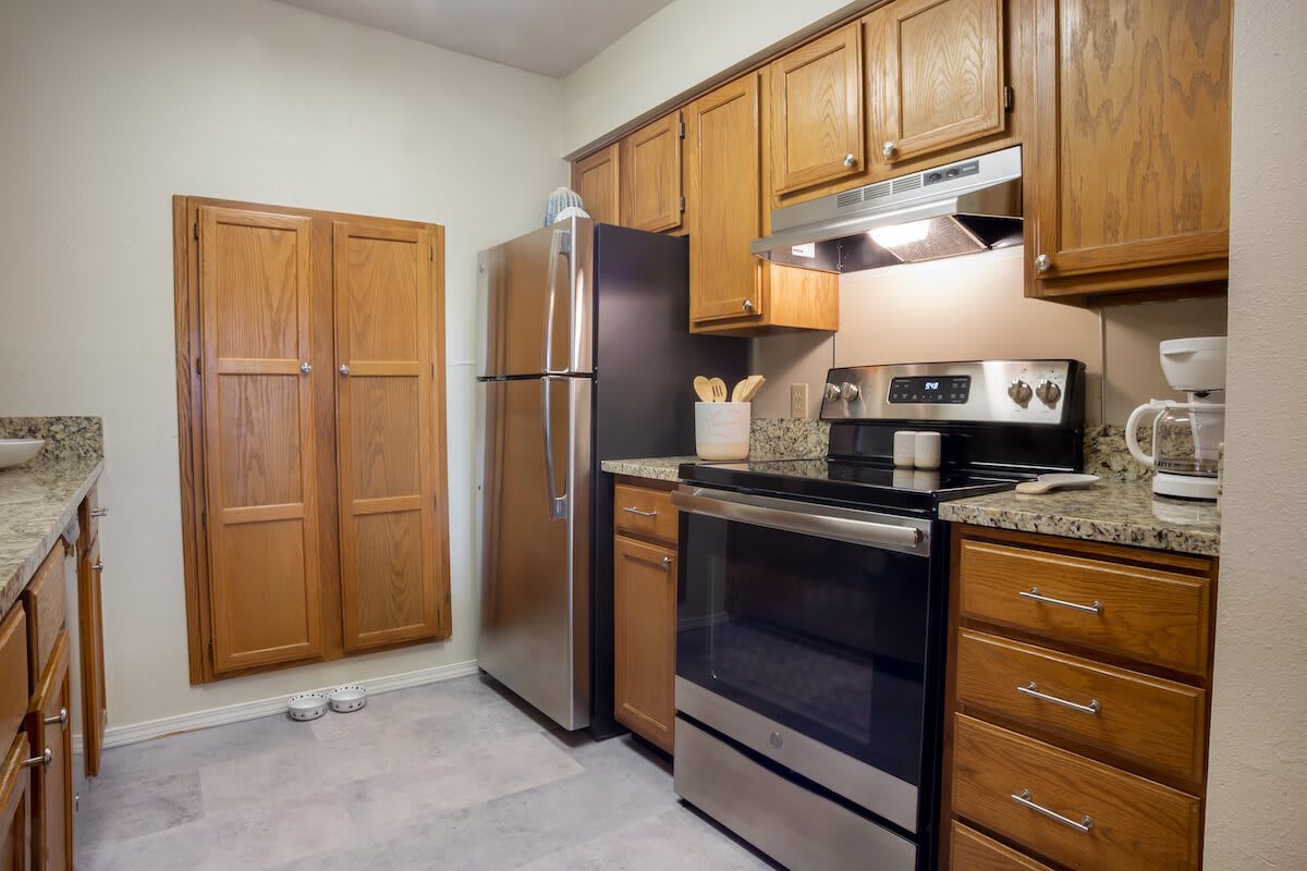 A kitchen with wooden cabinets, a stainless steel refrigerator, and an electric stove with oven.