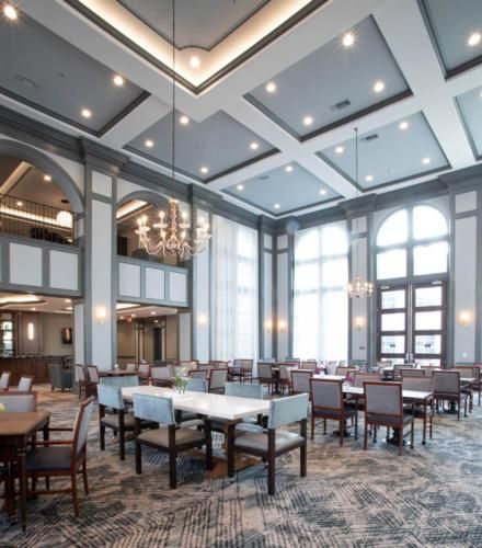 A spacious dining area with modern interior design, featuring high ceilings and elegant chandeliers.