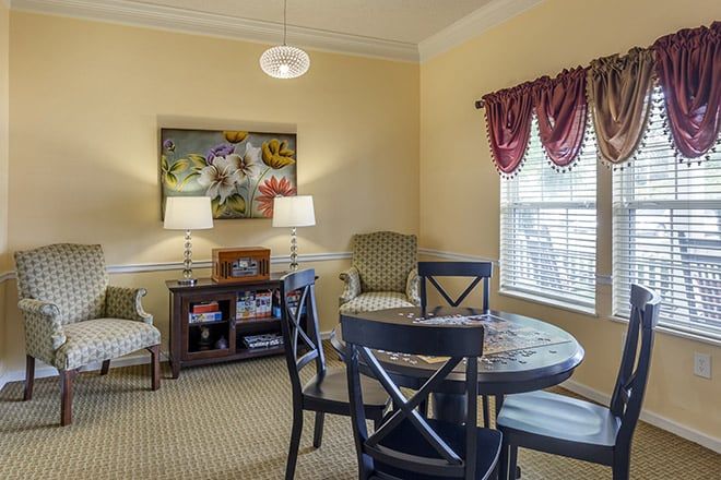 A cozy living room with a table and chairs, decorated with lamps, artwork, and curtains.