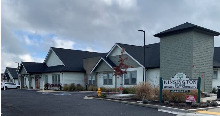 A modern building with a cloudy sky in the background, surrounded by a parking lot and minimal landscaping.