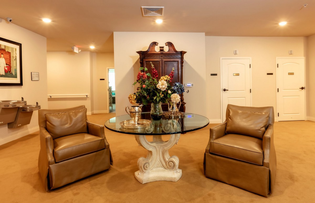 A cozy living room with two brown armchairs and a glass-top table adorned with flowers.